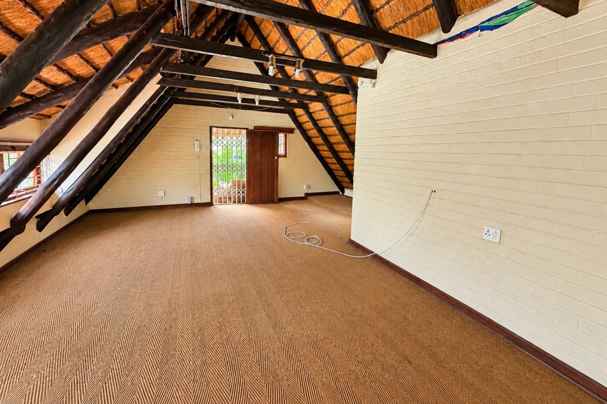 Spacious attic-style bedroom featuring exposed timber rafters, a thatched roof, and textured brick walls, offering a unique architectural character.