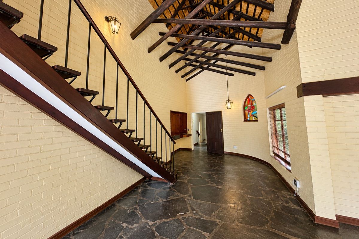 Spacious living area featuring high vaulted ceilings with exposed timber trusses, flagstone flooring, and a feature staircase.