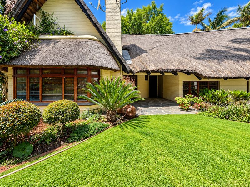 Charming cottage-style home featuring a traditional thatched roof, brick facade, and a stone-paved entrance surrounded by a well-maintained garden.