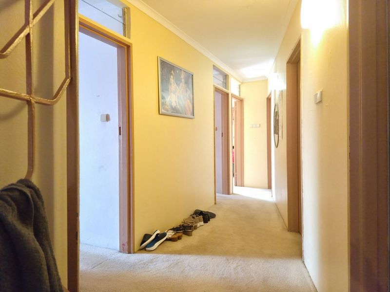 A long residential hallway featuring neutral wall paint, carpeted flooring, and multiple internal door access points.