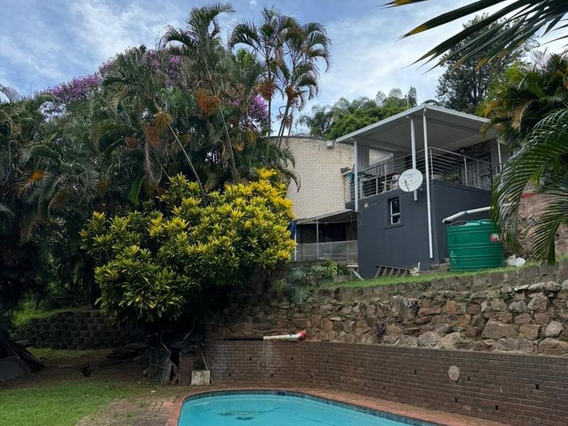 Outdoor pool area featuring a swimming pool, brick retaining wall, paved surround, and a raised covered patio with metal railings.