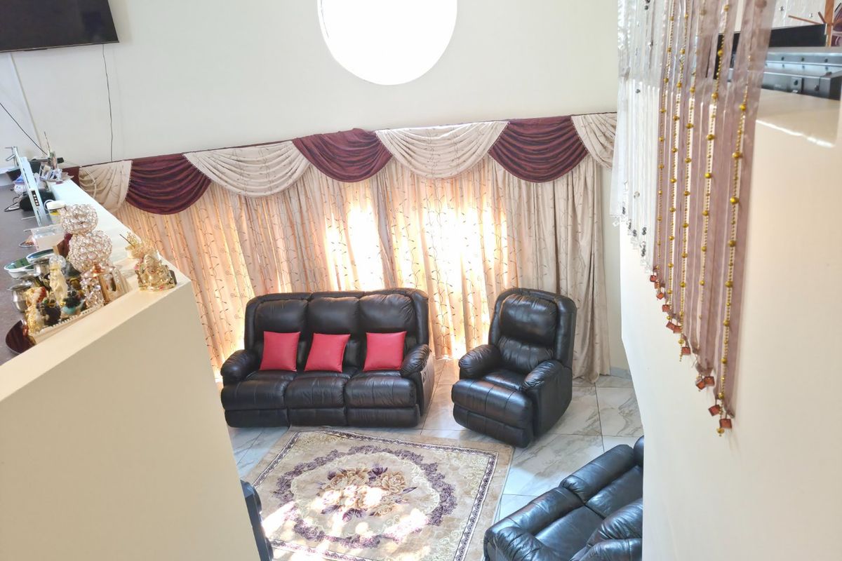 A spacious living room featuring high ceilings, a distinctive circular window, and tiled flooring, viewed from an elevated mezzanine level.