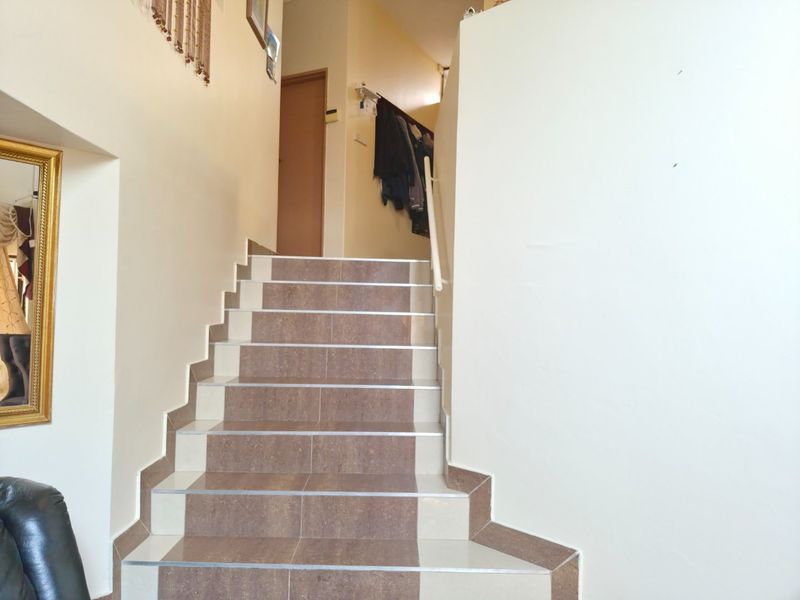 A bright hallway featuring a tiled staircase with a metal handrail leading to an upper level.