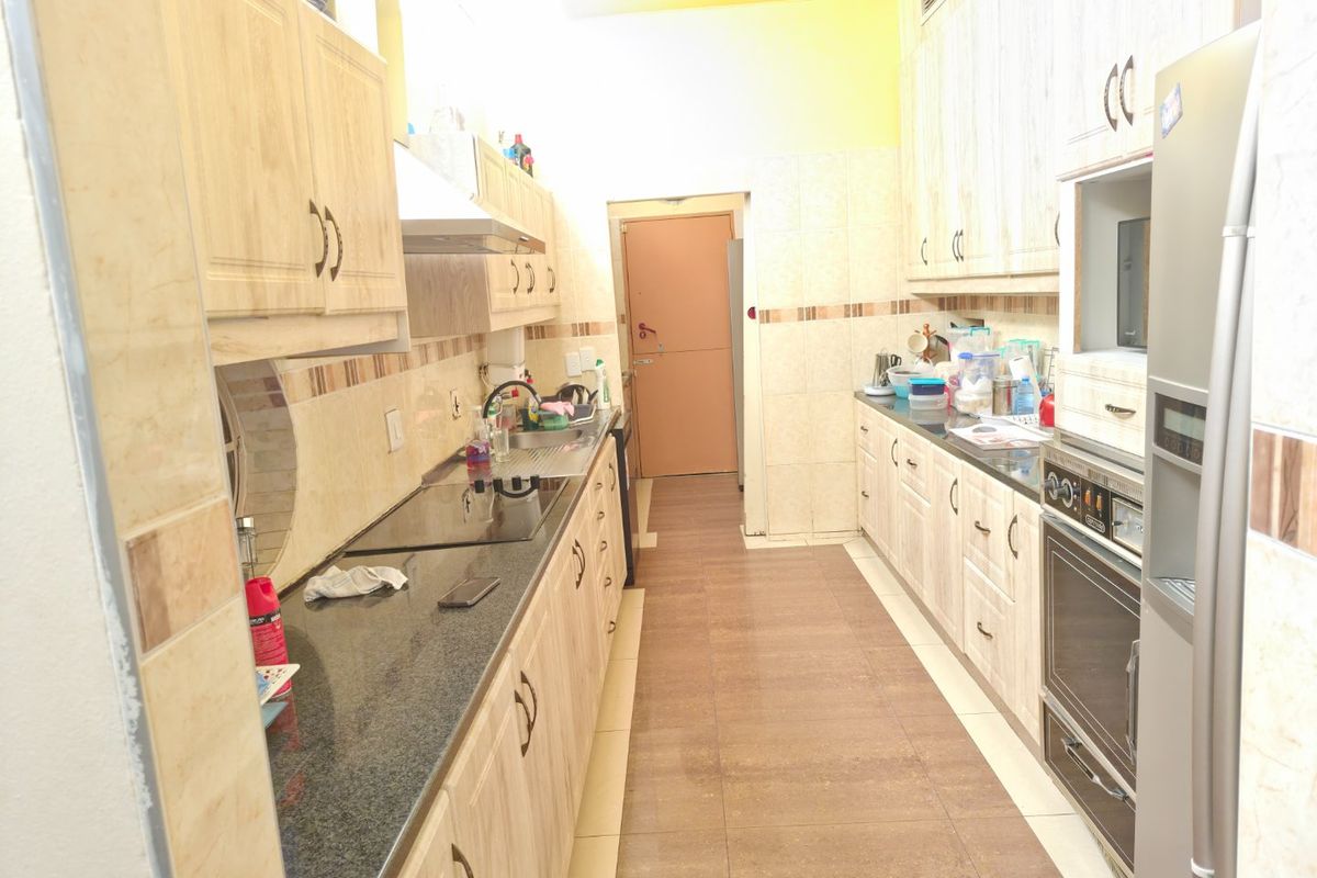 A functional galley-style kitchen featuring light wood-grain cabinetry, granite countertops, built-in oven, and a ceramic hob with an extractor fan.