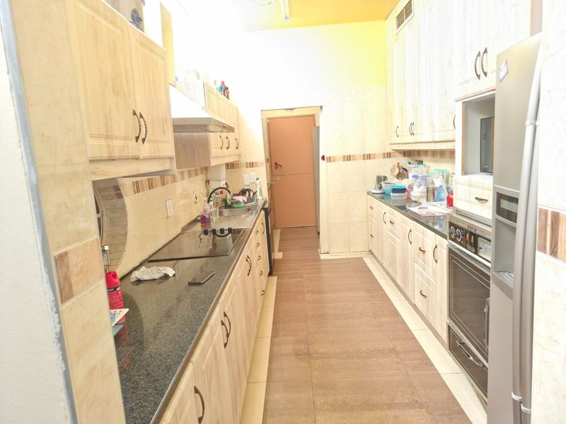 A functional galley-style kitchen featuring light wood-grain cabinetry, granite countertops, built-in oven, and a ceramic hob with an extractor fan.