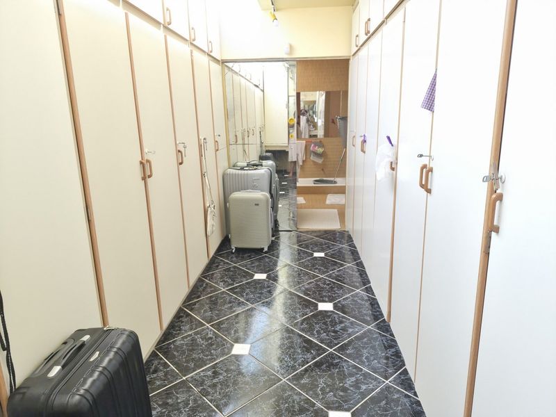 A narrow hallway featuring extensive built-in floor-to-ceiling storage cabinetry and dark patterned tile flooring, leading to a mirrored end wall.