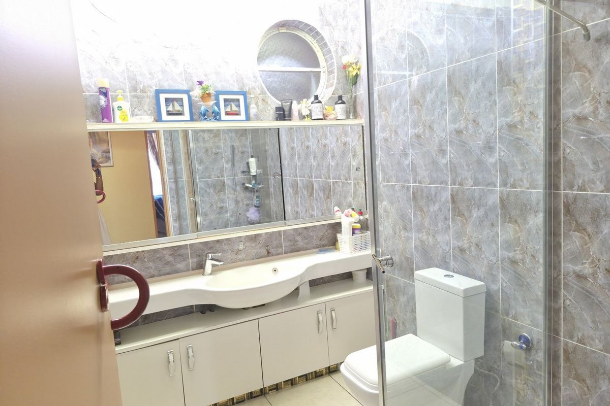 A functional bathroom featuring a vanity with integrated basin, glass shower enclosure, toilet, and full-height marble-effect wall tiling with a unique circular window.