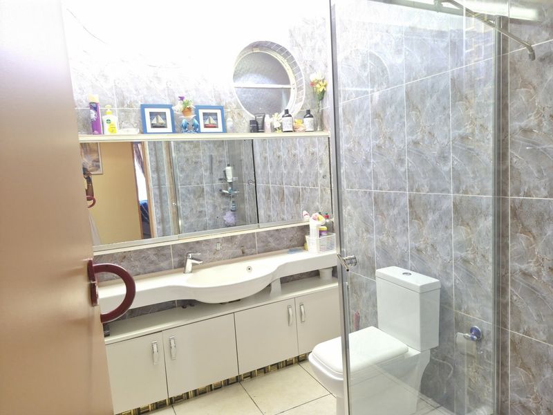 A functional bathroom featuring a vanity with integrated basin, glass shower enclosure, toilet, and full-height marble-effect wall tiling with a unique circular window.