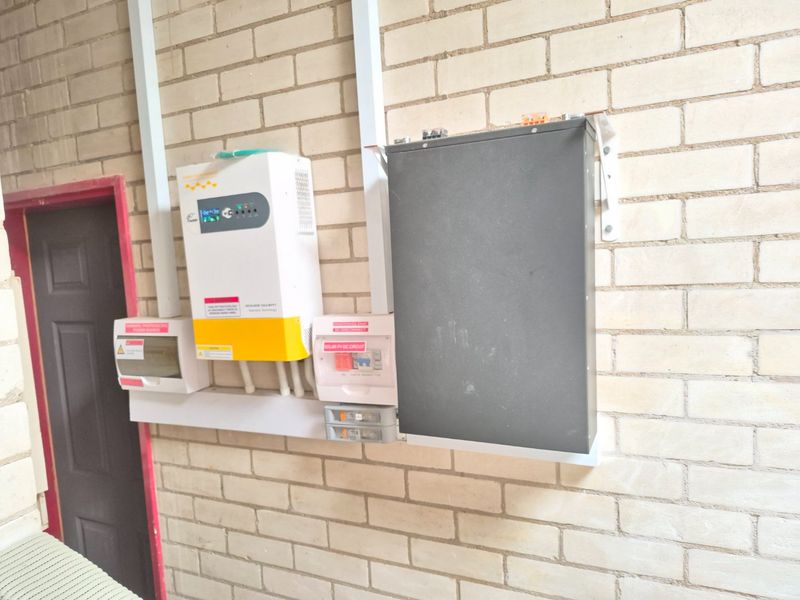 Utility area featuring a wall-mounted solar inverter system and electrical distribution board against an exposed brick wall.