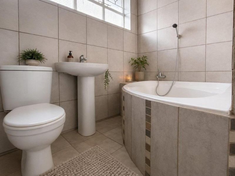 A well-maintained bathroom featuring a pedestal basin, toilet, and a tiled built-in bathtub with a handheld shower mixer.