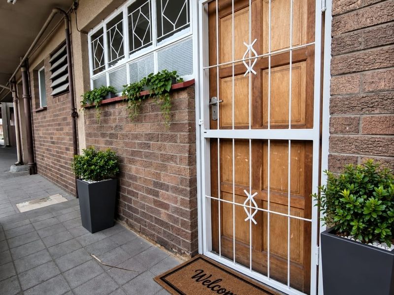 Entrance area featuring a solid timber door with a white security gate, set against a brick facade with tiled flooring.
