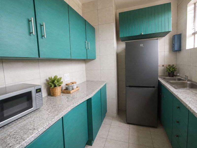 A functional kitchen featuring teal cabinetry, granite countertops, a double basin sink, and neutral tiled finishes throughout.