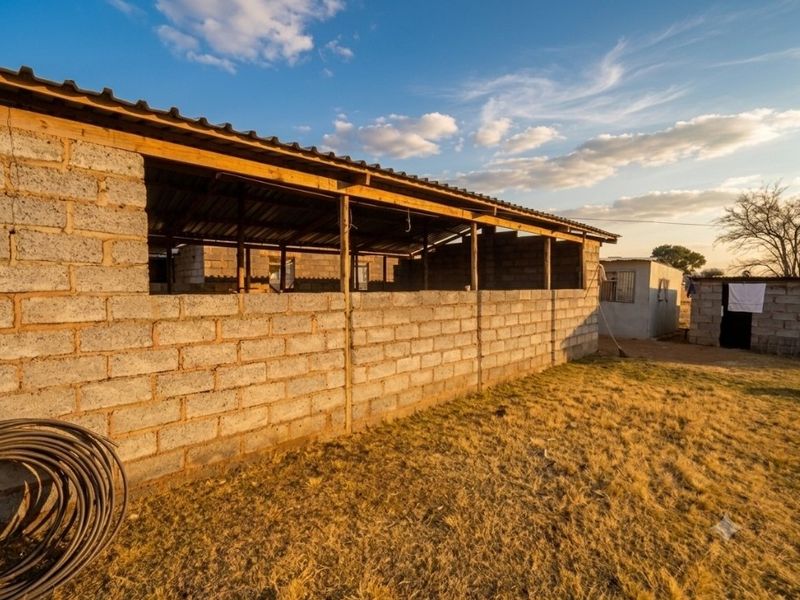 An unfinished open-sided farm structure featuring cinder block walls and a corrugated metal roof, set within a rural landscape.