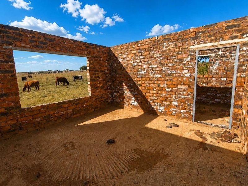 An unfinished structure featuring exposed brick walls and a metal door frame, currently in a shell state with dirt flooring.