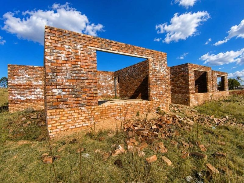 An unfinished brick structure showing the exterior shell and foundation on a rural property lot.
