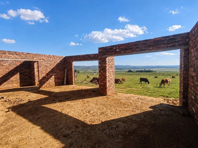 An unfinished brick structure under construction, featuring open wall frames and expansive rural views across the farm landscape.
