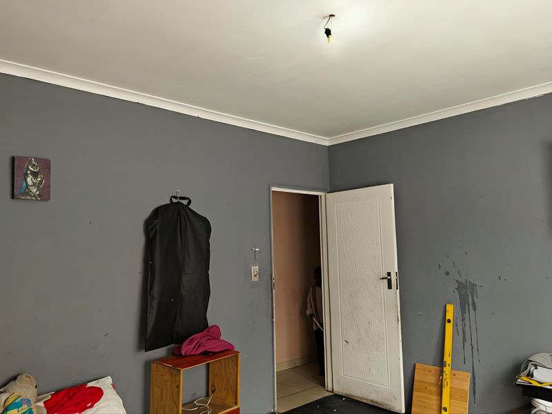 A bedroom featuring grey painted walls with visible surface damage and staining, requiring cosmetic attention and repair to the ceiling light fixture.