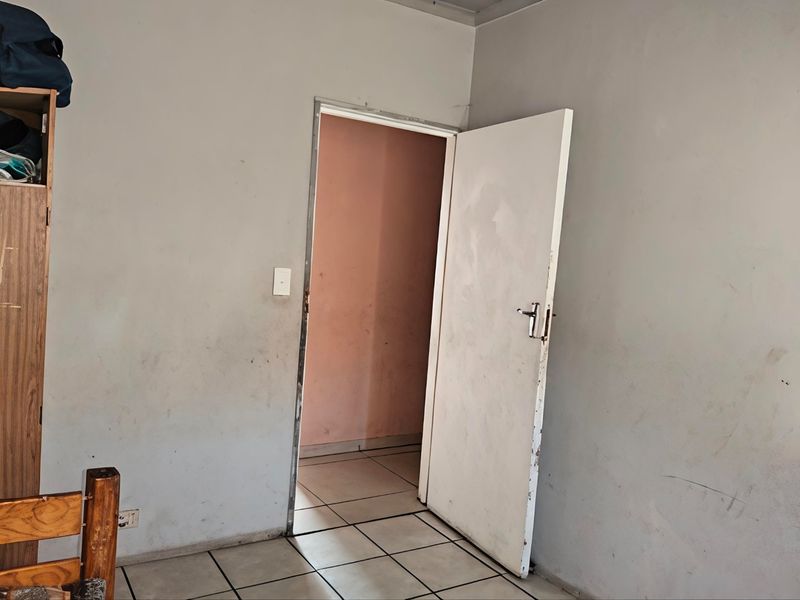 A vacant bedroom featuring tiled flooring and a doorway leading to an adjacent space, requiring cosmetic updates to the walls and door.