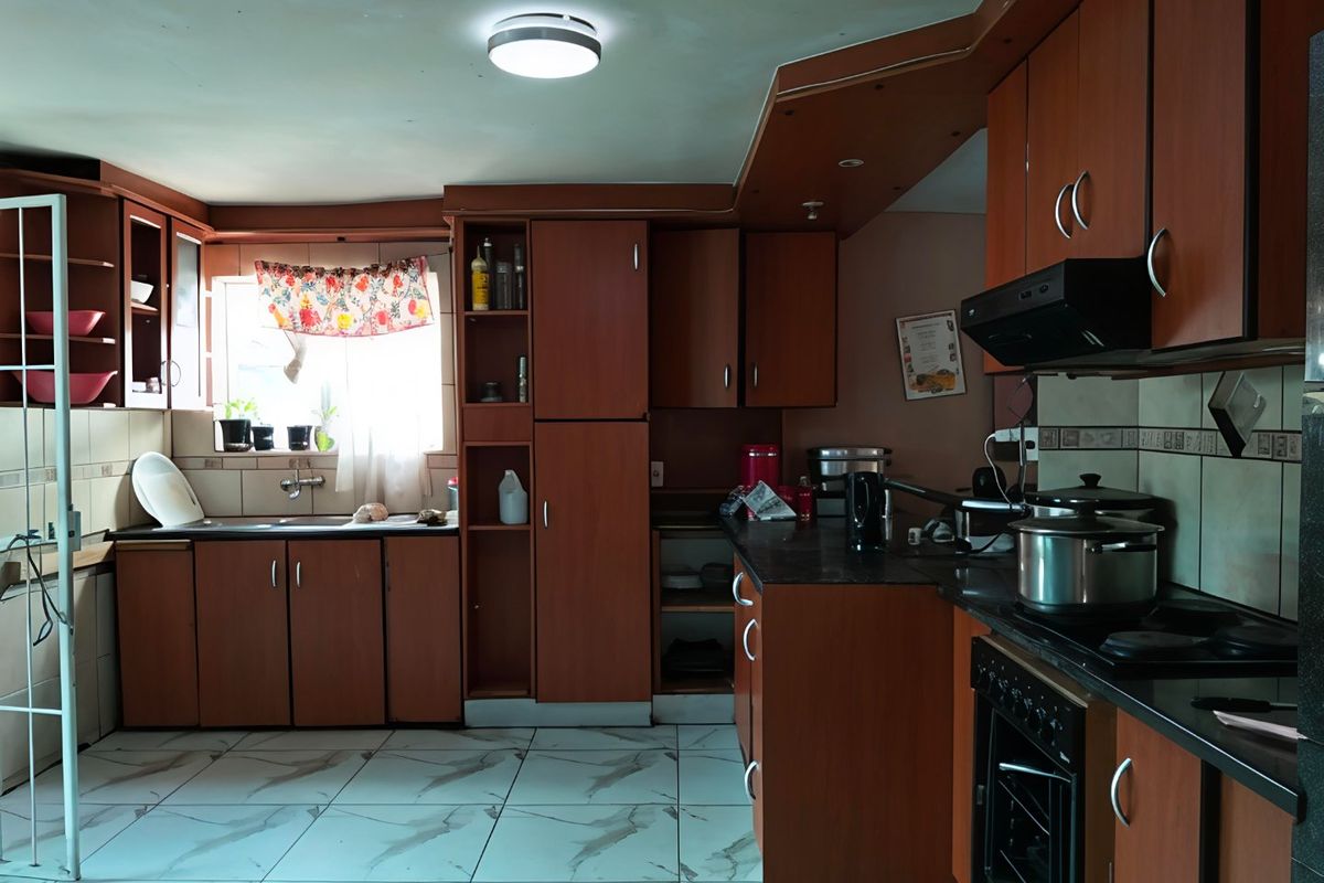 A functional kitchen featuring wood-tone cabinetry, dark countertops, built-in oven and hob, and tiled flooring, offering potential for a modern update.