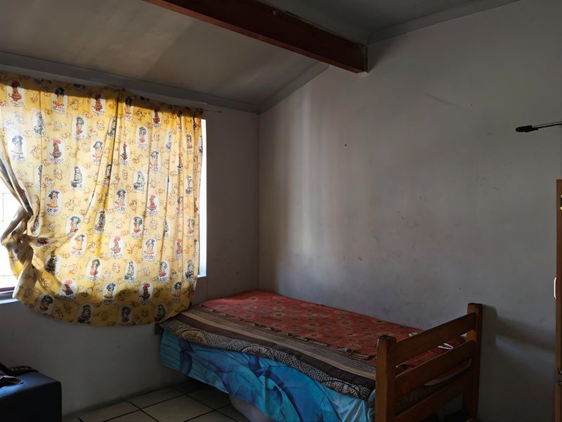 A bedroom featuring tiled flooring and an exposed ceiling beam, currently showing signs of wear on the wall surfaces.