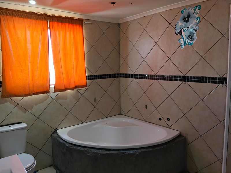 Bathroom featuring a corner bathtub, toilet, and tiled walls. The space requires finishing touches including faucet installation and completion of the bathtub base.