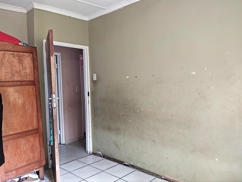 A bedroom interior featuring tiled flooring and coved ceilings, currently requiring wall repairs and repainting to restore the space.
