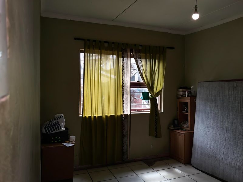 A sparsely furnished bedroom featuring tiled flooring and a window, requiring cosmetic updates to improve its overall appeal and condition.