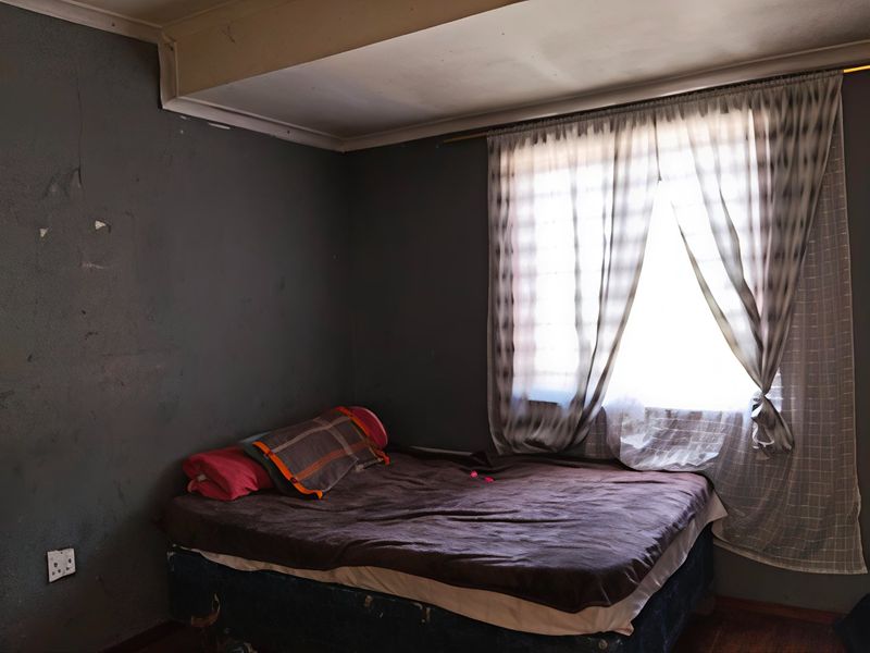 A bedroom featuring dark painted walls with visible plaster cracks and a window with curtains.