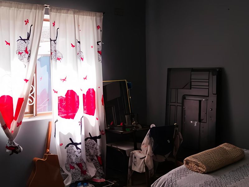 A bedroom featuring dark painted walls and natural light entering through a window with patterned curtains.