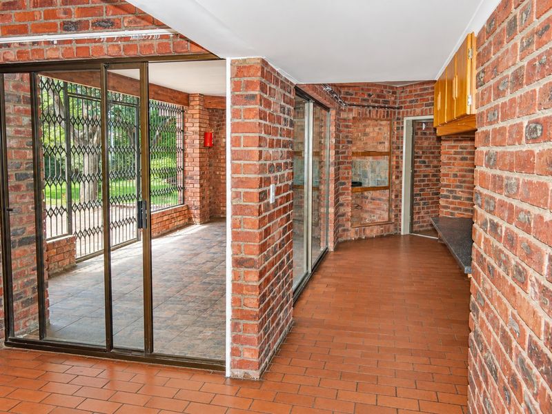 Spacious covered patio featuring exposed brick walls, tiled flooring, and built-in cabinetry, providing a versatile outdoor entertainment area with secure sliding door access.