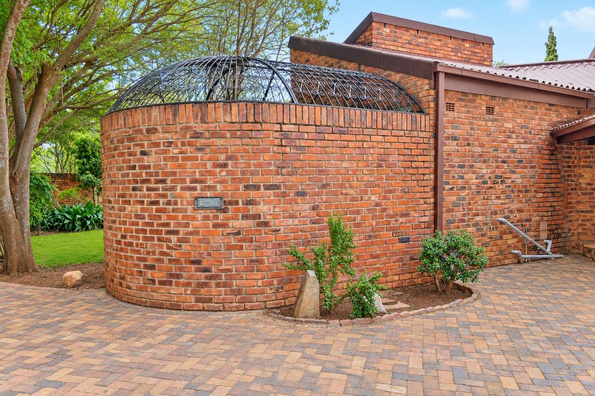 A unique architectural feature with a curved face brick wall and decorative wrought iron dome, set against a paved courtyard area.