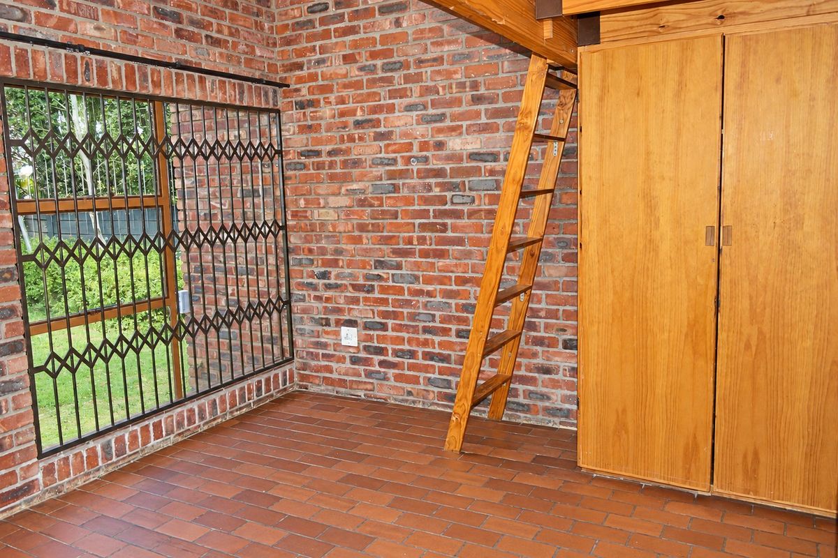 A bedroom featuring exposed brick walls, tiled flooring, a built-in wooden wardrobe, and a wooden ladder leading to a loft area.