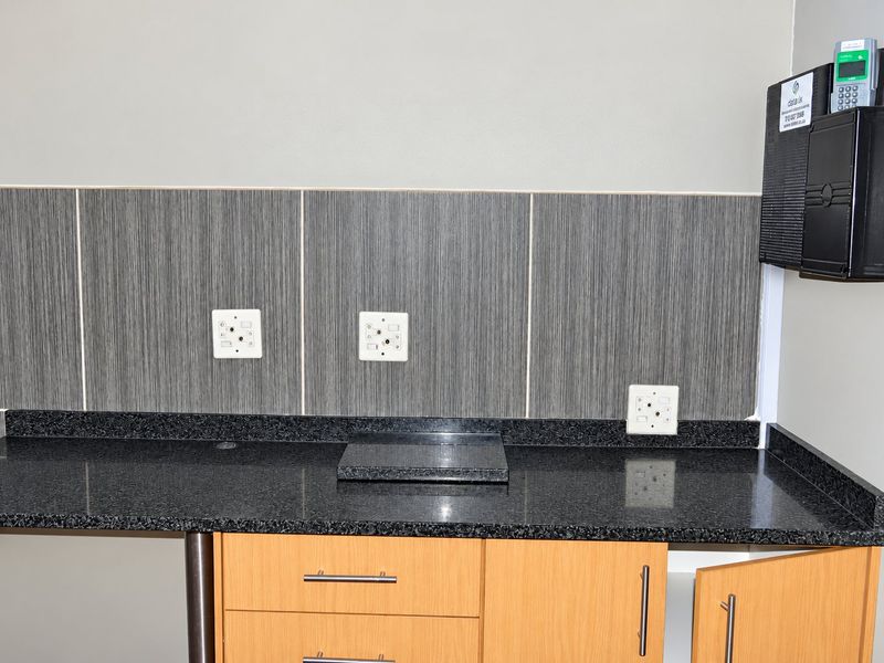 A functional scullery or utility area featuring granite countertops, wood-finish cabinetry, and a tiled backsplash with multiple electrical points.