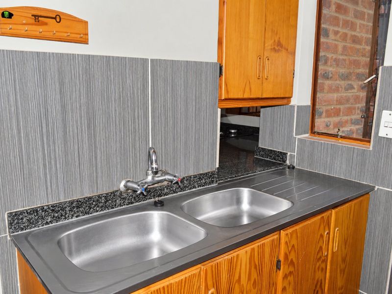 A functional scullery area featuring wooden cabinetry, a double stainless steel sink, granite countertops, and modern grey tiled backsplash.