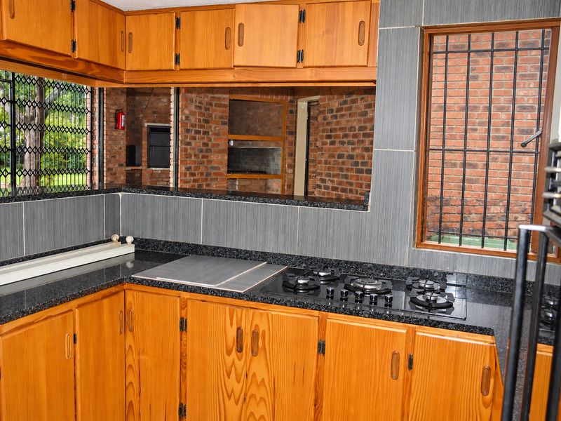 A functional kitchen featuring wooden cabinetry, granite countertops, and a built-in gas hob, with a view through to an outdoor brick-walled entertainment area.