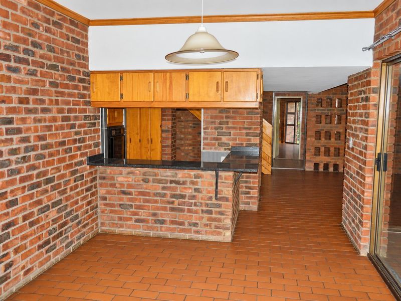 A dated kitchen area featuring exposed brick walls, built-in wooden cabinetry, a brick breakfast bar, and tiled flooring, offering potential for modern renovation.