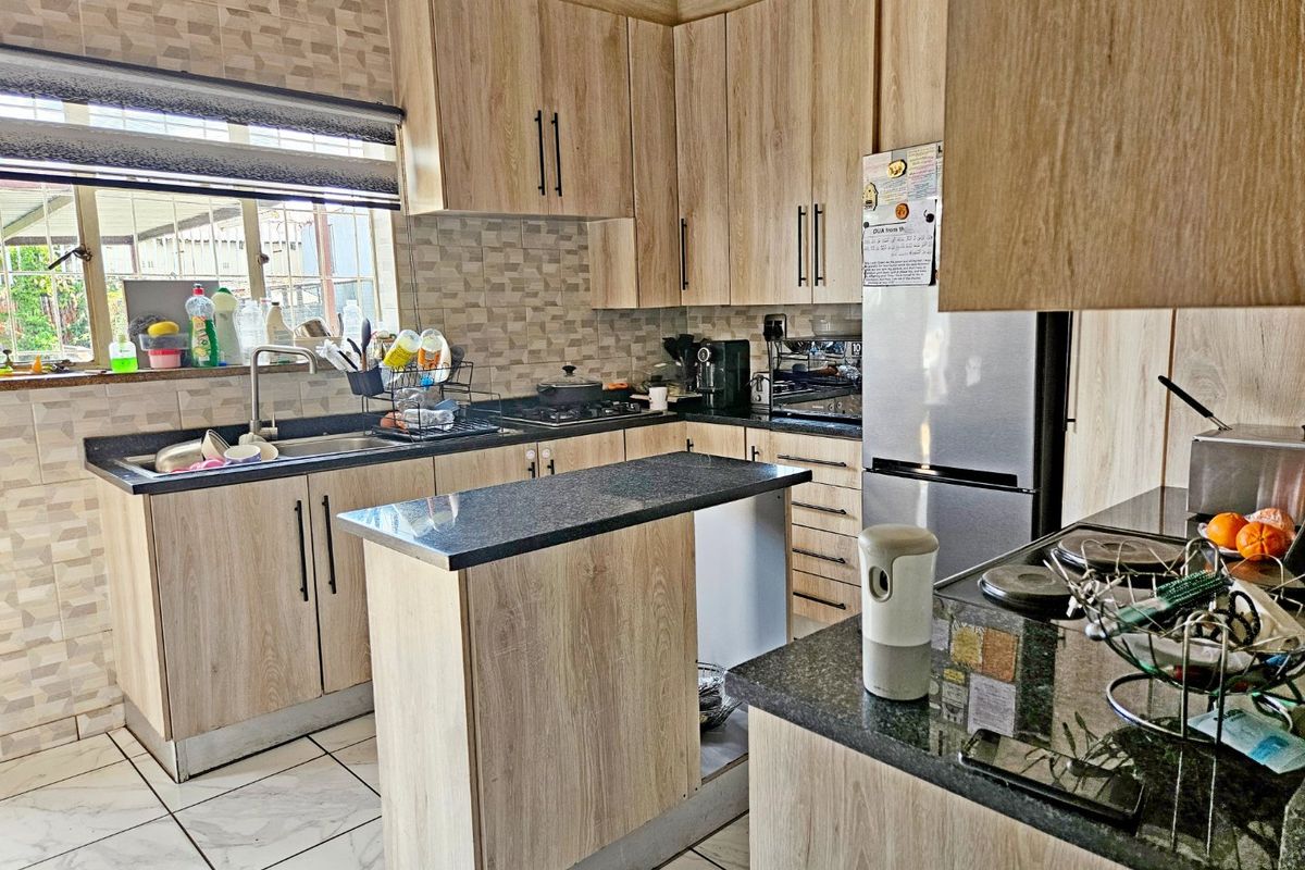 A functional kitchen featuring light wood-grain cabinetry, dark granite countertops, a gas hob, and tiled flooring with a neutral backsplash.
