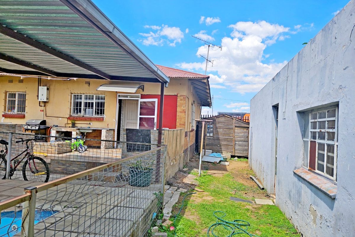 Rear exterior view showing a covered patio area with a built-in braai, adjacent garden space, and perimeter boundary walls.
