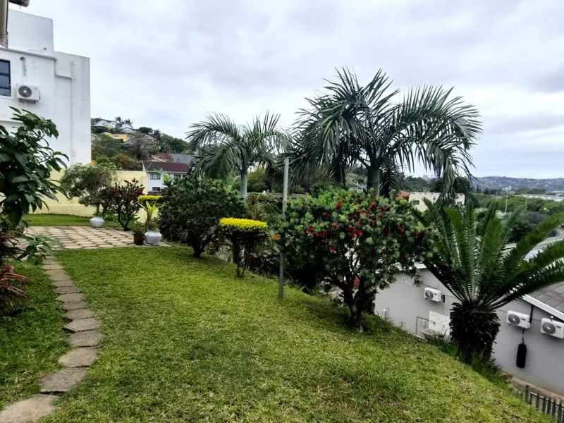 A view of the rear garden area featuring a brick exterior wall, paved pathway, and established landscaping overlooking the surrounding neighbourhood.