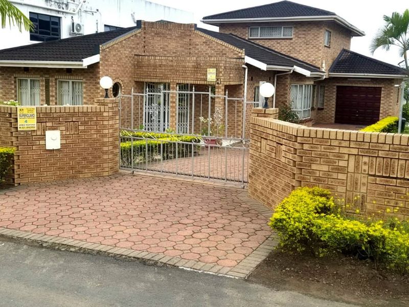 Front elevation of a face brick house featuring a paved driveway, secure perimeter wall with metal gate, and an integrated garage.