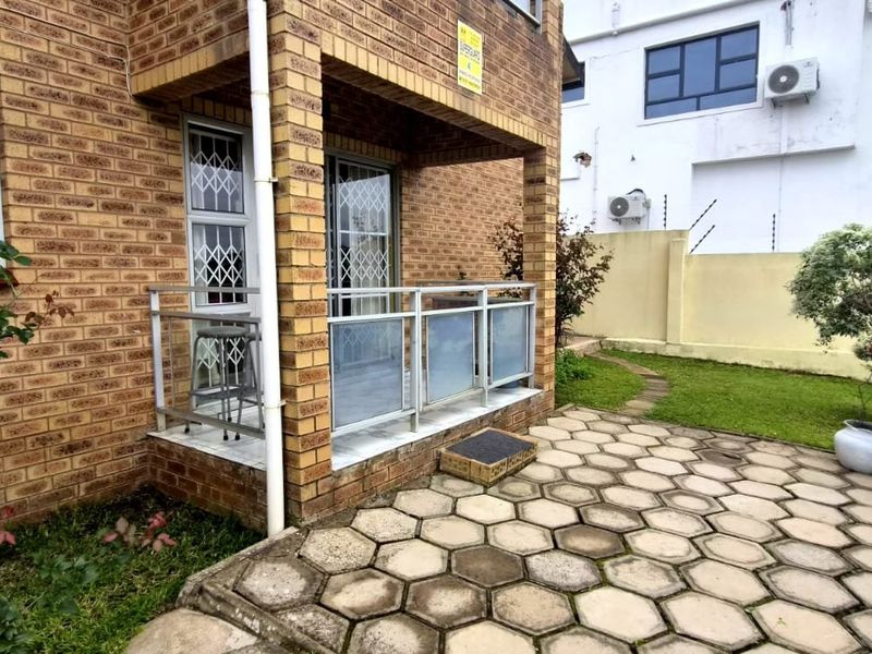 Rear exterior view featuring a face brick facade, a covered patio area with metal balustrades, and a paved garden space with electric fencing.