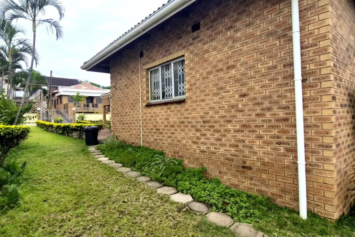 A side view of the property featuring face brick exterior walls, security window bars, and a landscaped garden area along the boundary wall.