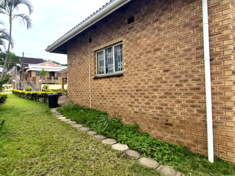 A side view of the property featuring face brick exterior walls, security window bars, and a landscaped garden area along the boundary wall.