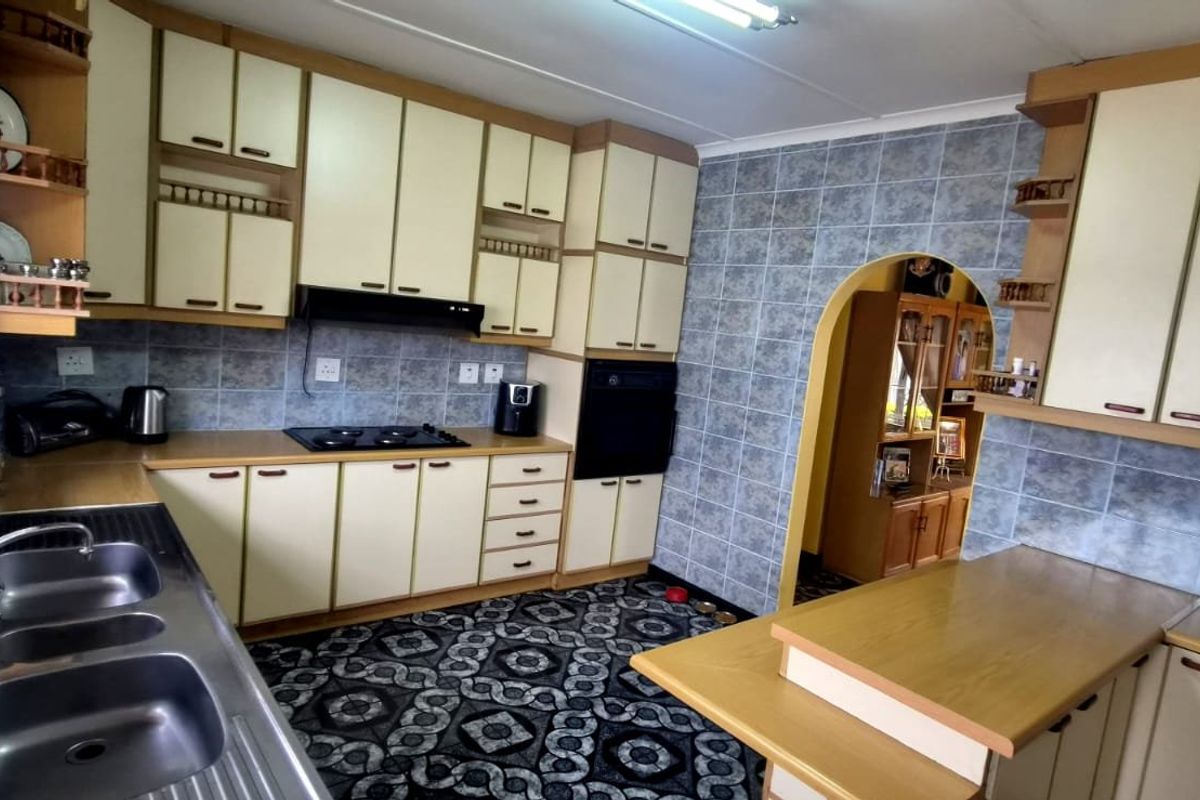 A dated kitchen featuring built-in cabinetry, a double sink, integrated oven, and hob, with tiled splashbacks and a breakfast counter.