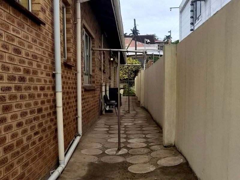 A narrow side passage featuring face brick exterior walls, paved flooring, and a high boundary wall with security electric fencing.