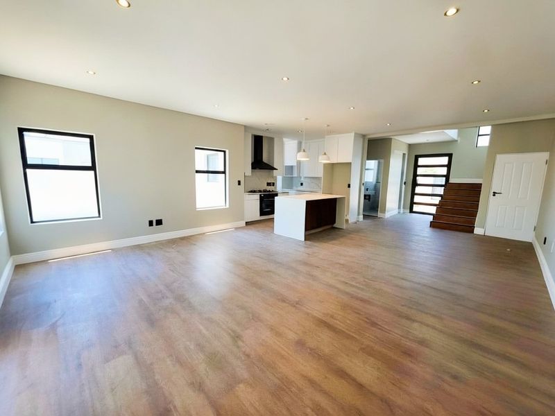 Spacious open-plan living area featuring modern laminate flooring, recessed lighting, and a sleek kitchen with a central island and built-in appliances.