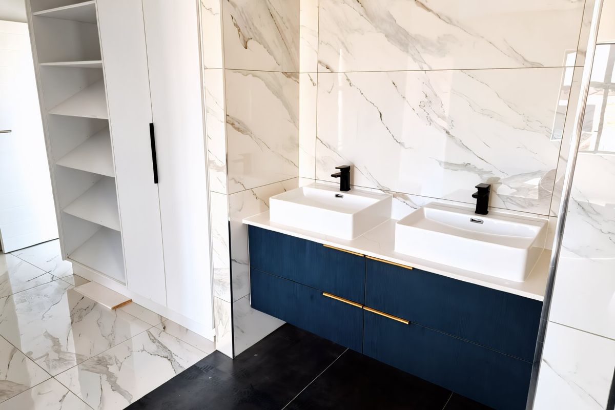 Modern bathroom featuring a sleek double vanity with vessel sinks, black fixtures, and elegant marble-look wall tiling with integrated storage shelving.