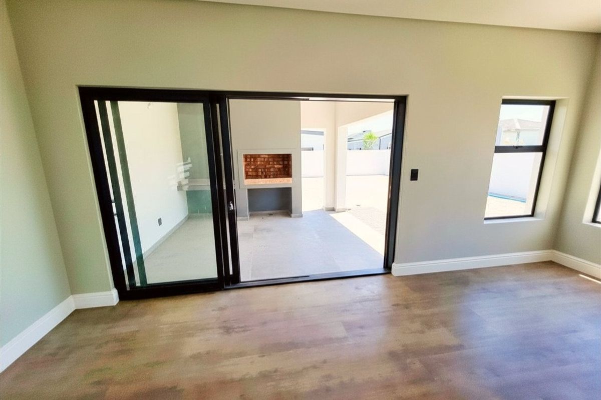 Bright living area featuring modern laminate flooring and large sliding doors opening onto a covered patio with a built-in braai.