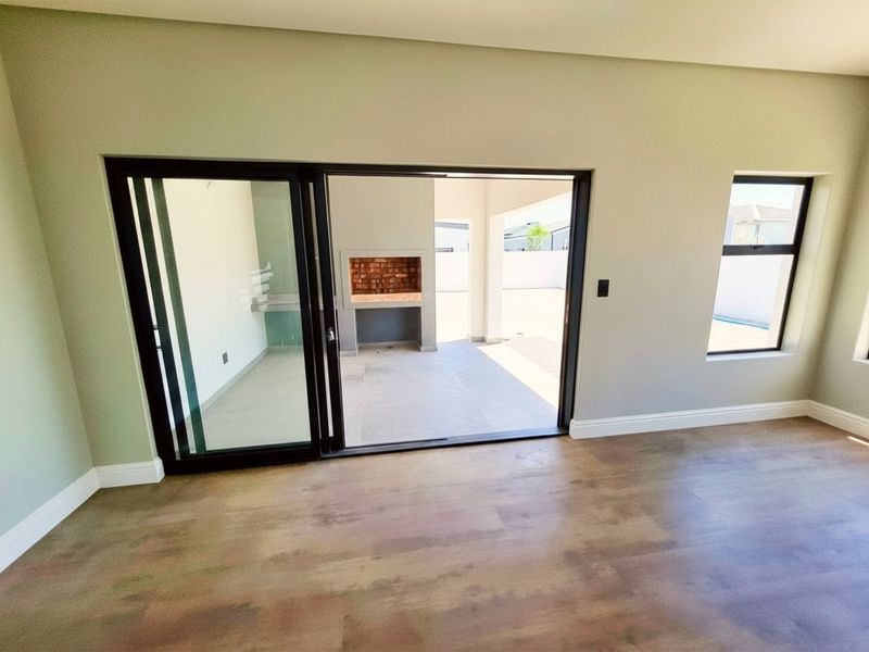 Bright living area featuring modern laminate flooring and large sliding doors opening onto a covered patio with a built-in braai.