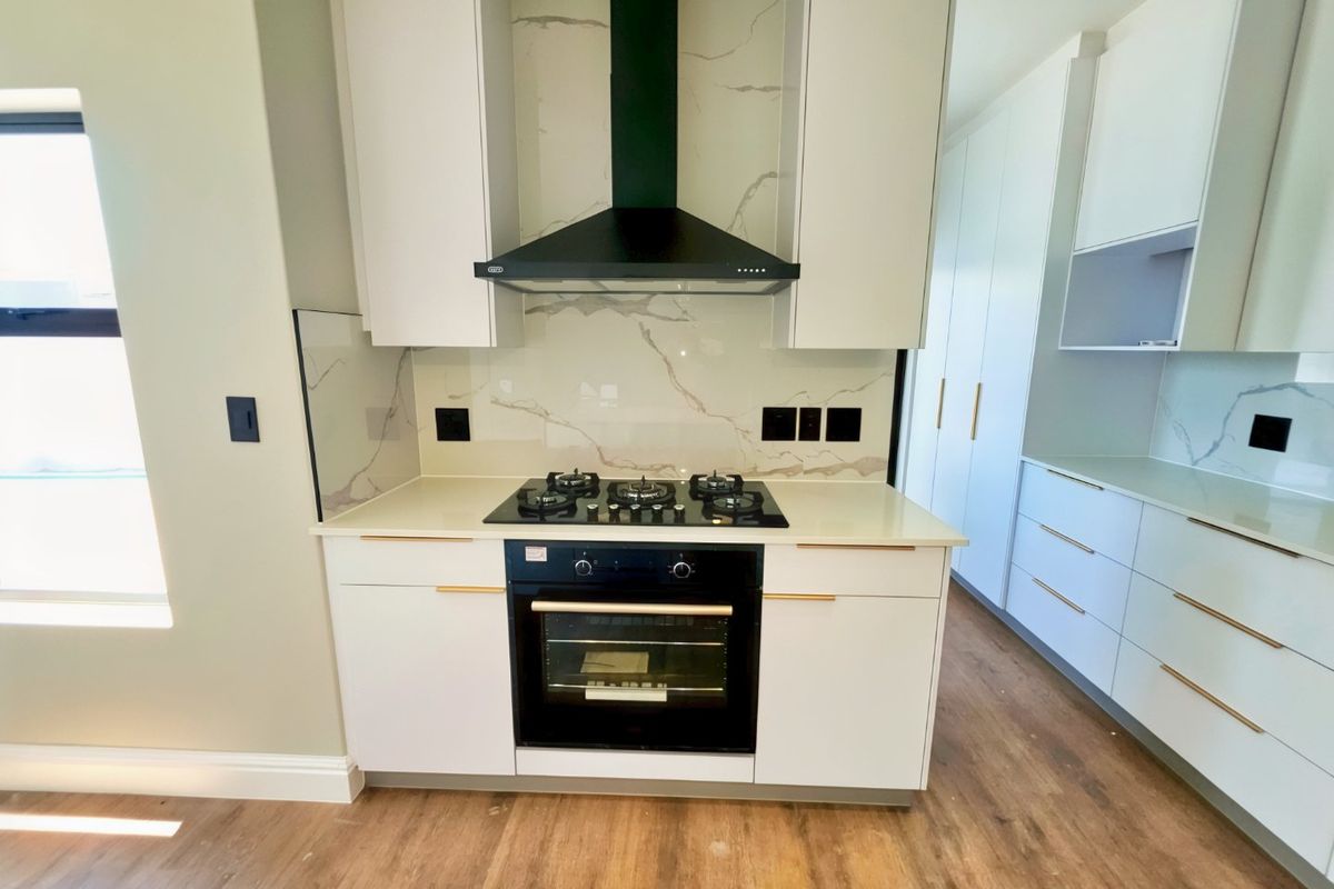 Modern kitchen featuring sleek white cabinetry, stone countertops, marble-look splashback, and high-quality built-in gas hob and oven.